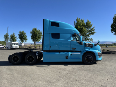 Mack PR64T76H truck cab in blue side profile with sleeper, undercarriage and rear dual wheels visible in an open lot.