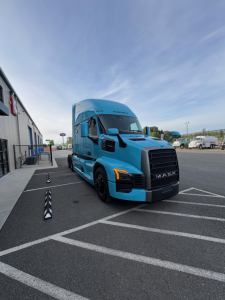 Black Mack PR64T76H tractor-trailer in blue parked in a lot showing front grille with MACK logo and cab height.