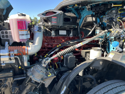 Mack PR64T76H engine bay showing red diesel engine, air intake, hoses, and various labeled reservoirs and components.