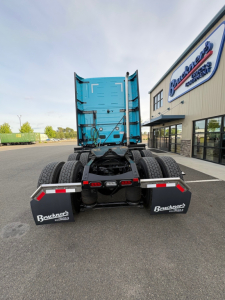 Truck rear view showing fifth-wheel and dual rear axles of a blue Mack PR64T76H tractor in a dealership lot.