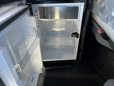 New Mack PR64T76H sleeper cab truck interior showing open compact refrigerator/freezer with shelves and door bins in cabin area.