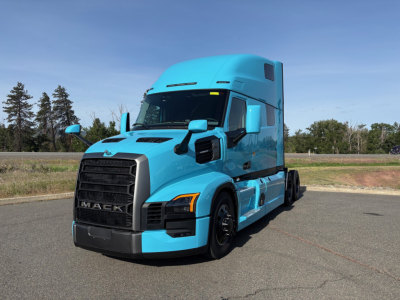 Truck cab exterior showing 2027 Mack PR64T76H teal blue conventional sleeper tractor with large grille and aerodynamic mirrors.