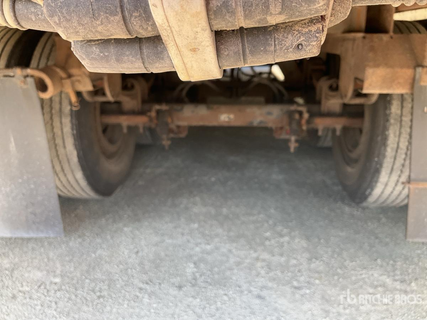 Underneath view of a trailer showing tandem wheels and suspension components, dirt and grime on frame and components.