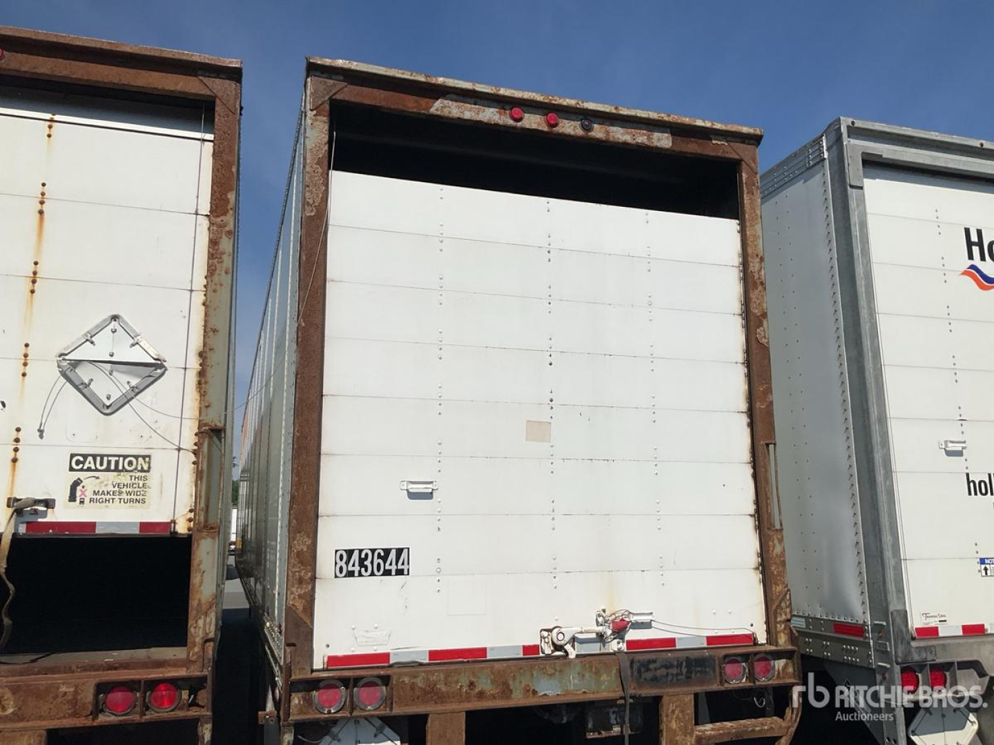Back of a white trailer with a rusted frame showing rear doors and a black number plate 843664 on the door.