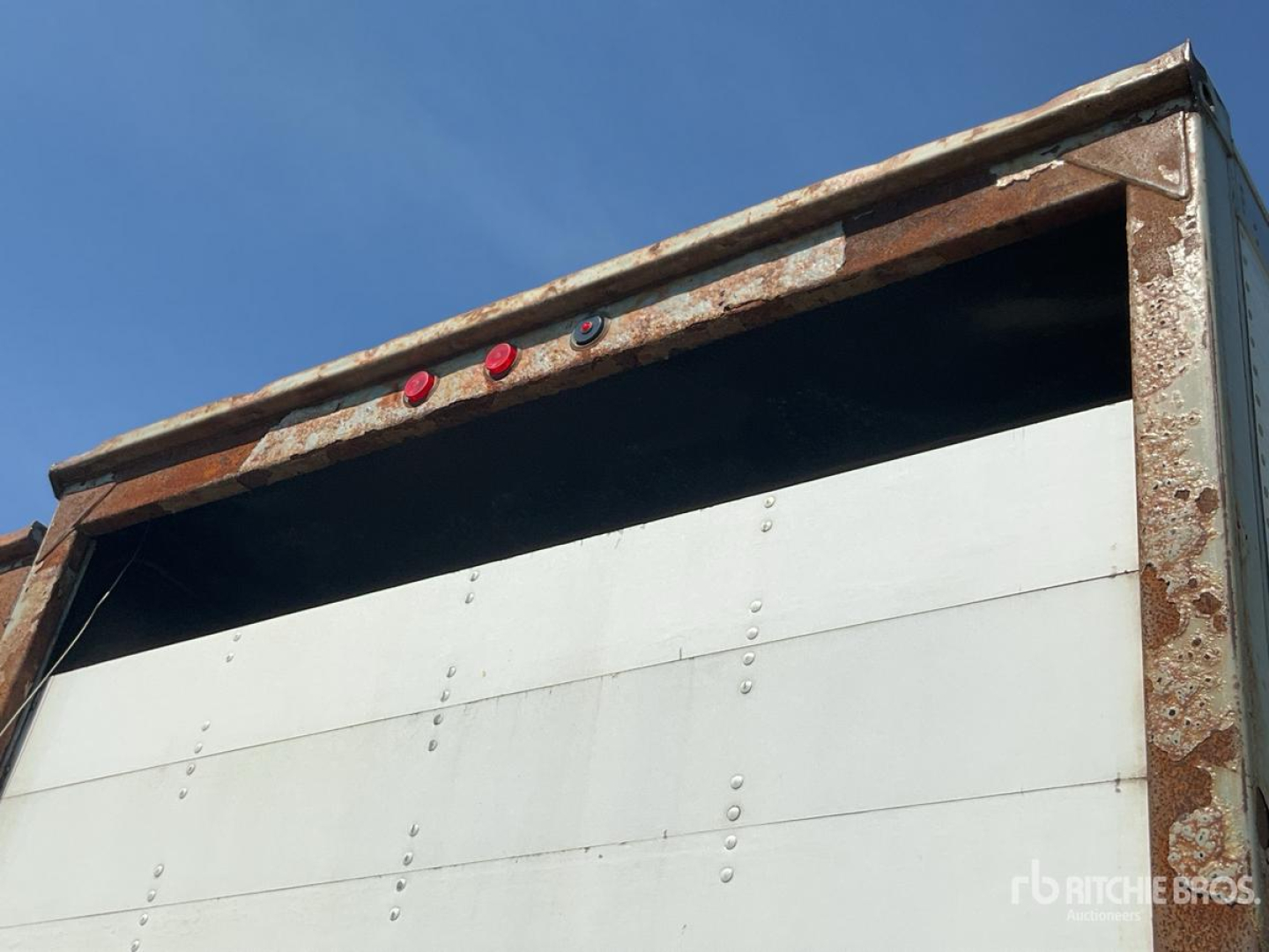 Trailer rear opening showing rusted frame and white segment panels with riveted joints.