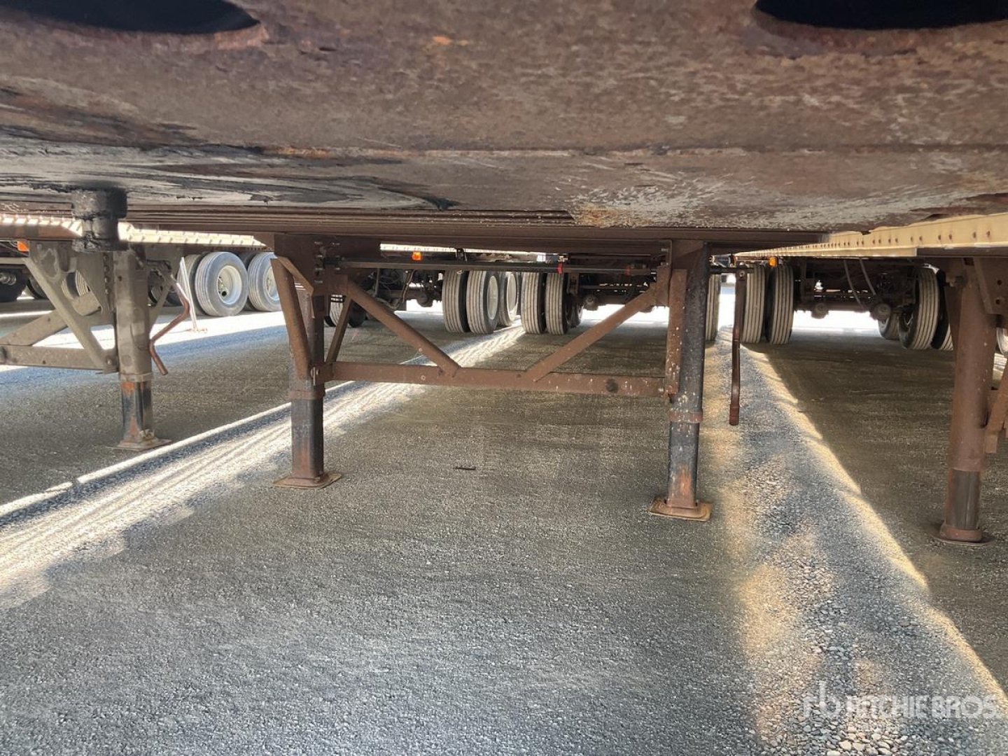 Trailer undercarriage showing leaf springs and support jacks with axle and wheel assemblies in the background.