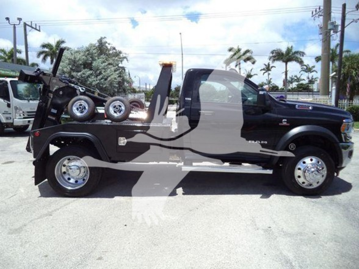 Ram 5500 SLT tow truck side view showing spare wheel, tow hoist, and winch undercarriage with black body and chrome wheels.