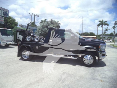 Ram 5500 SLT flatbed tow/utility truck parked sideways showing dual rear wheels and winch with front crew cab, dark blue body, chrome wheels.