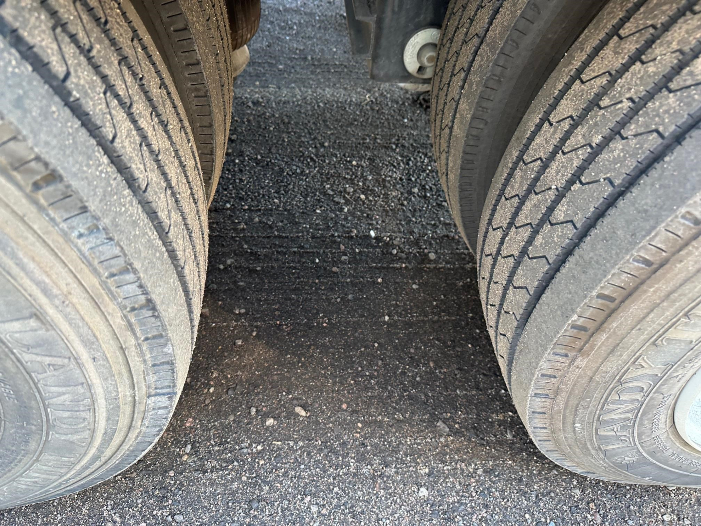 Dual rear wheels of a trailer show tires with treads, viewed from between the axles on a drop deck trailer.