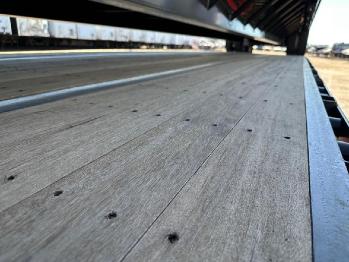 Trailer flatbed deck with wood planks and steel edges; close-up view of Dura Haul steel closed tandem drop deck trailer bed showing wood texture and fastener dots.