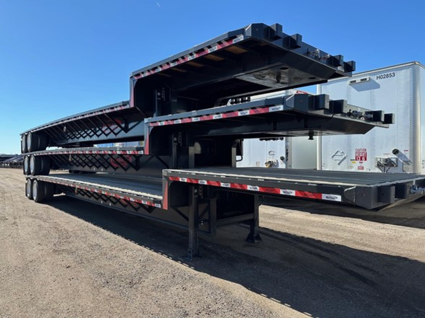 Steel closed tandem drop deck trailer stacked in slots with multiple levels and ramps visible.