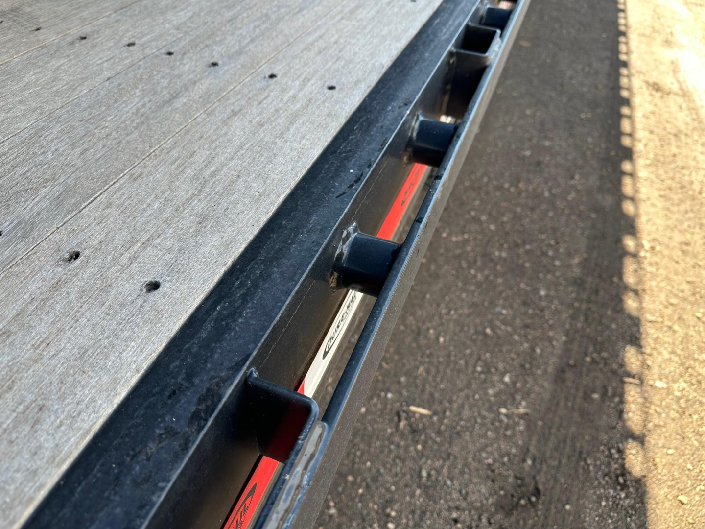 Flatbed trailer deck edge with rollers and hardware showing metal surface and support brackets in view.