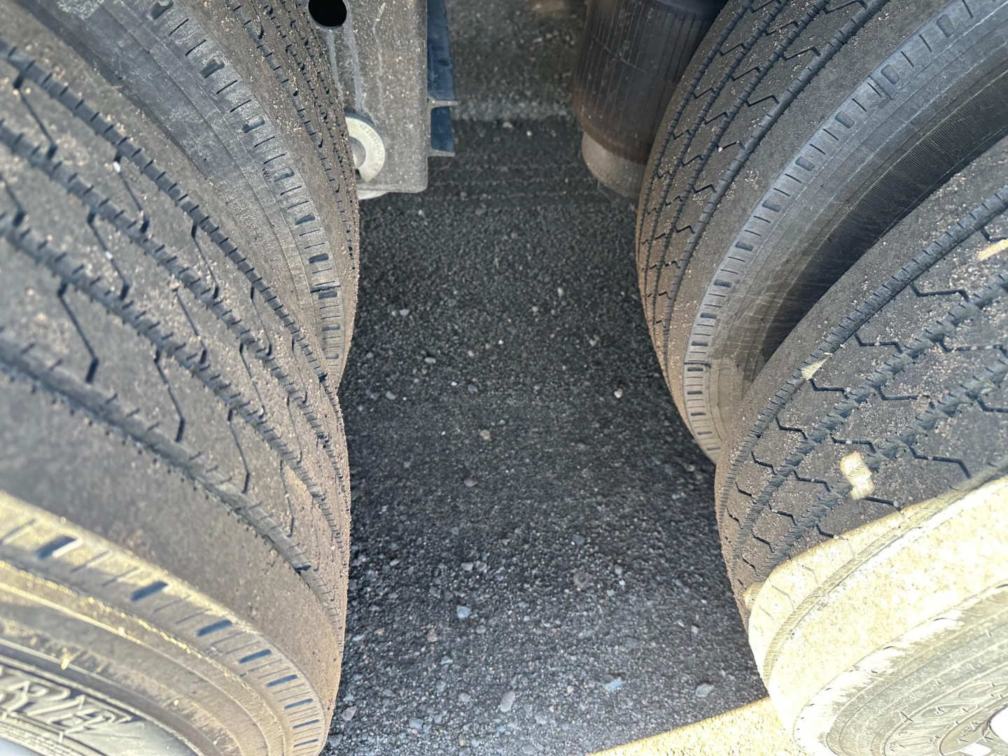 Truck trailer tires and mud guard viewed from between tandem axles on a Dura Haul closed tandem drop deck trailer.