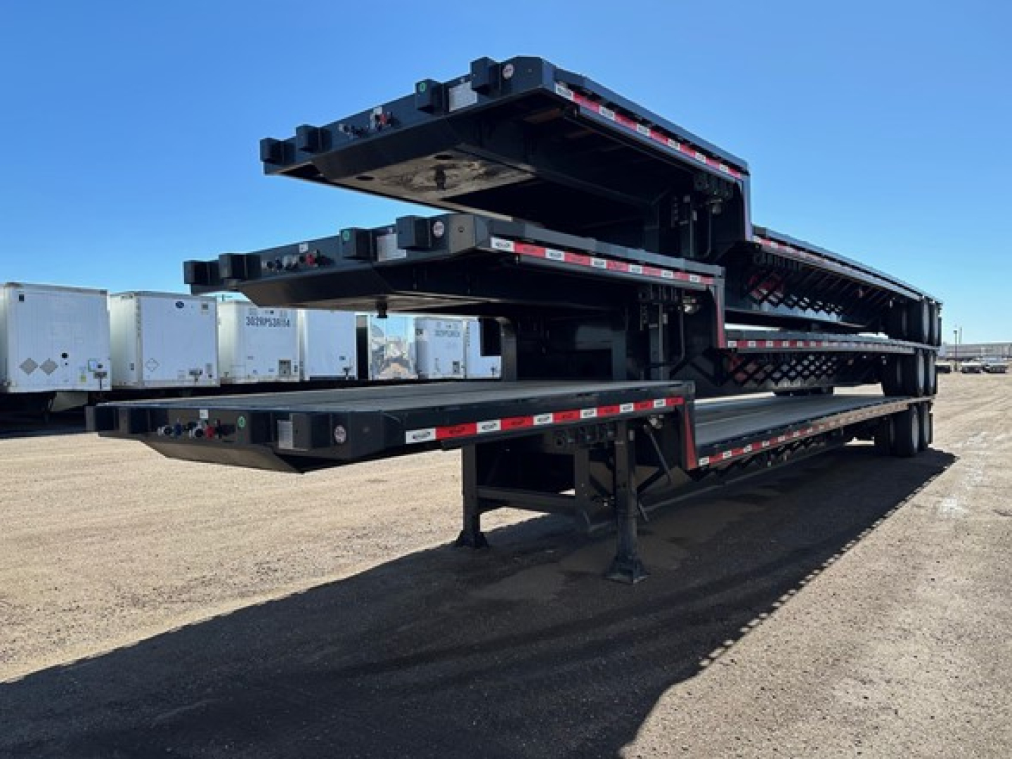 Trailer stack of a Dura Haul drop deck trailer with multiple tiers folded, showing black frame and reflective red/white safety tape along edges.