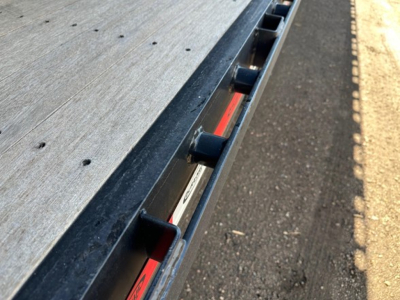 Close-up view of a steel closed tandem drop deck trailer edge with rails and mounting hardware along the side.