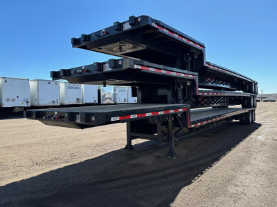Flatbed trailer with stacked drop decks, black steel, with reflective tape along edges and support legs visible.