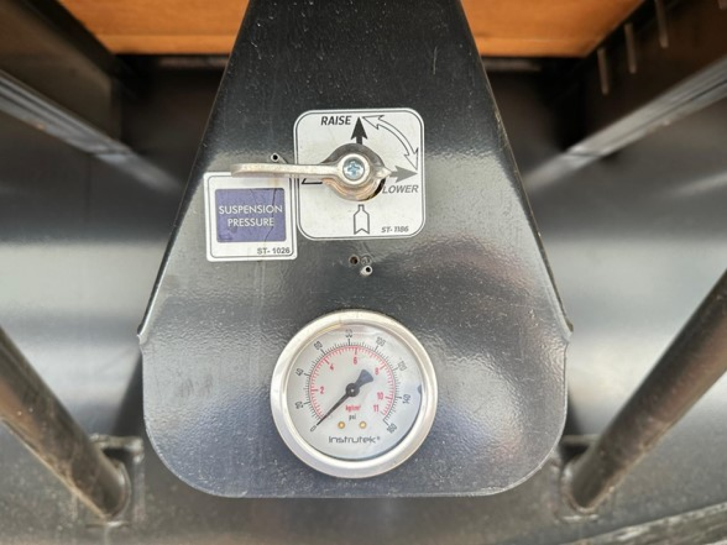 Drop deck trailer control panel with suspension pressure gauge and calibration sticker showing 'RAISE' and 'LOWER' arrows, analog gauge at bottom.