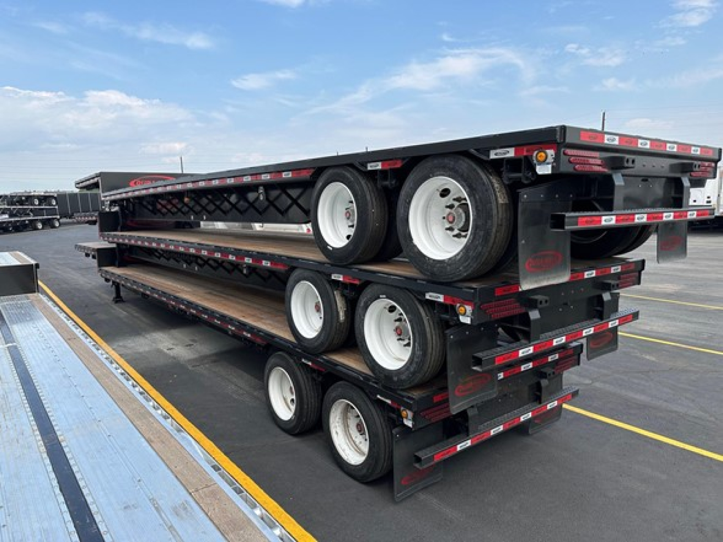 Trailer stack showing multiple flatbed drop deck trailers with wheels and frames stacked on top of each other.