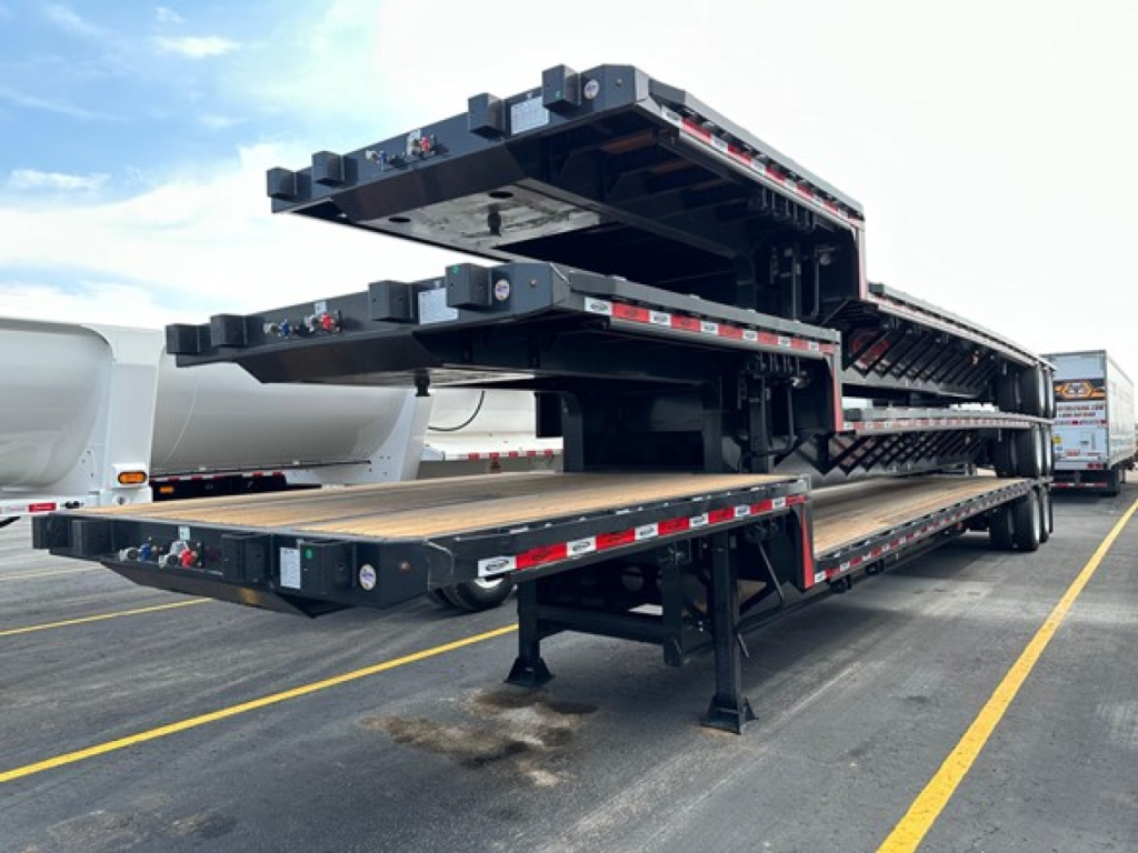 A multi-level stack of black drop deck trailers with stacked platforms and support legs, viewed from side with clear warning reflectors.