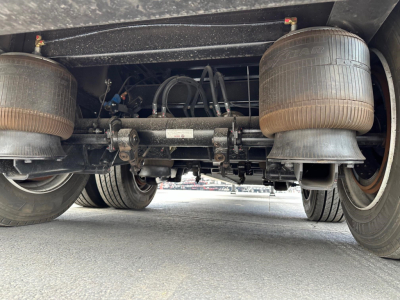 Rear underside of trailer showing dual axles, suspension beam, air lines, and two large round air tanks.