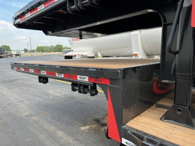 Trailer deck with drop deck and wood plank surface; rear undercarriage and support beams visible; black and red safety decals along edge.