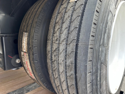 Trailer wheel and tire 9R Allied light gray rim with treaded tires mounted on a trailer, viewed from side showing dual tires and part of chassis.
