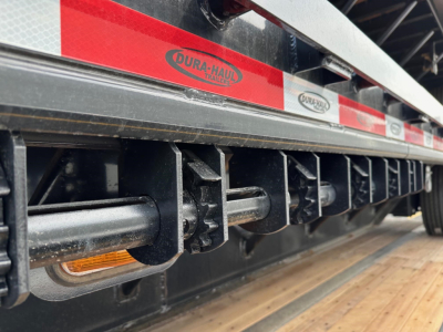 Trailer deck side showing Dura-Haul Trailer logo and reflective red/white stripes with undercarriage beams and lighting along the edge.