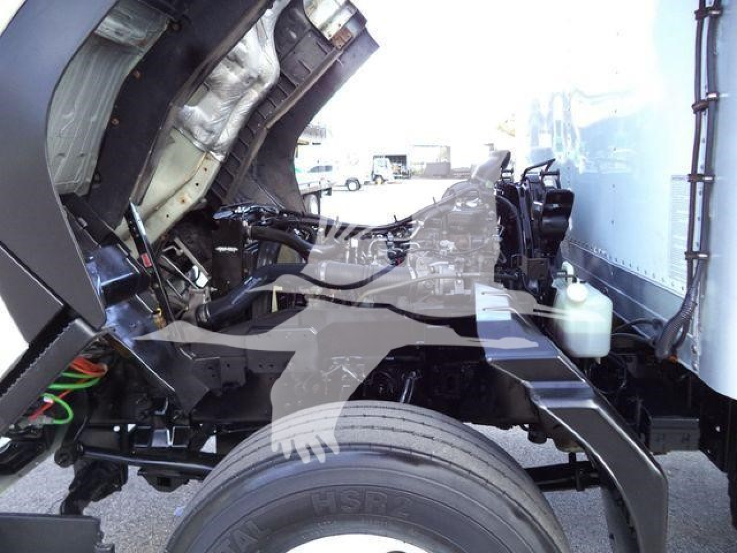 Isuzu FTR truck cab and chassis area showing front wheel, suspension, and empty engine bay with some wiring and fluid reservoirs visible.