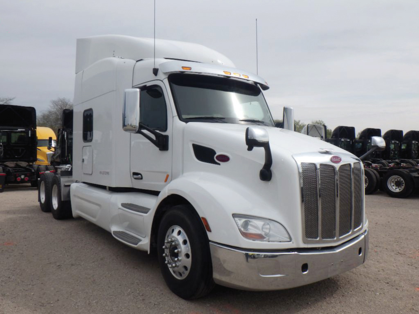 Peterbilt 579 UltraCab semi-truck in a lot, front three-quarter view showing large chrome grille, white exterior, sleeper cab, and dual rear axles.