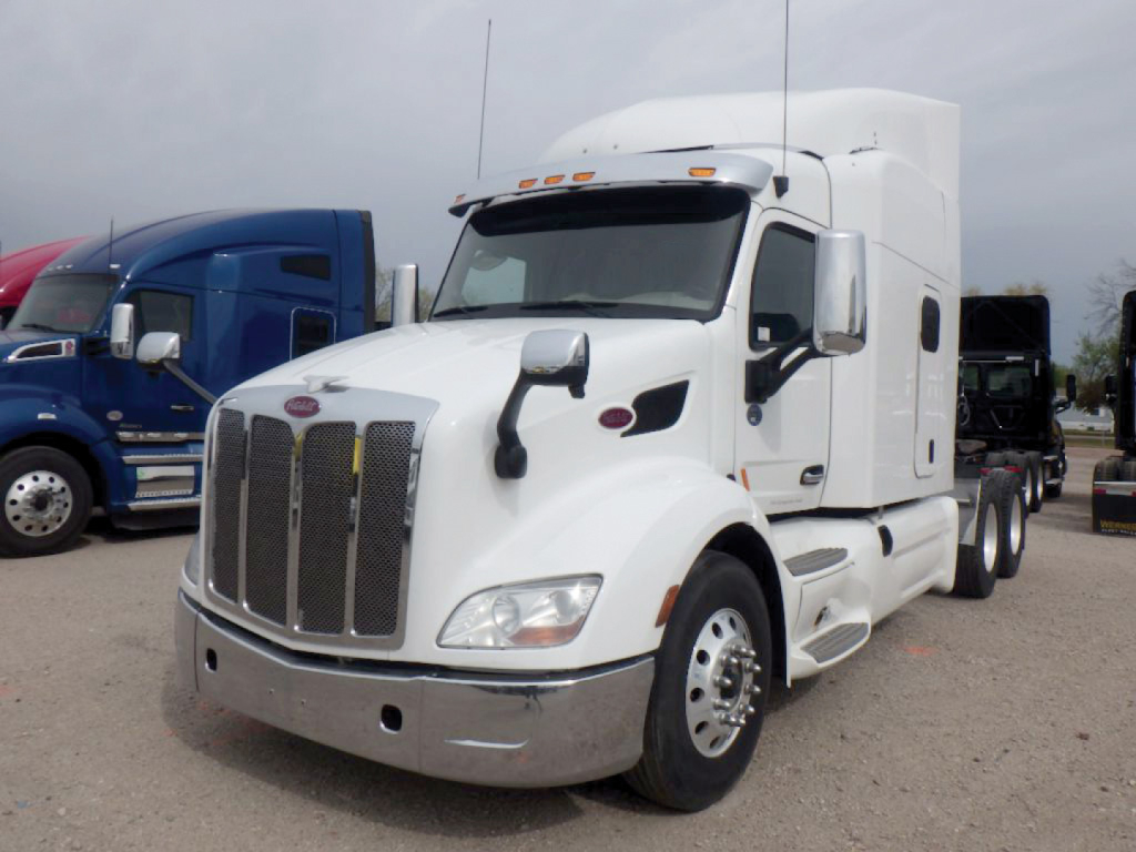 Peterbilt 579 UltraCab tractor in a lot, white exterior with chrome grille and mirrors, front view showing cab and aerodynamic hood.