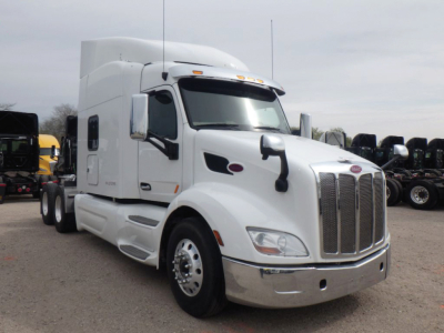 Peterbilt 579 UltraCab semi-truck in a lot, front three-quarter view showing large chrome grille, white exterior, sleeper cab, and dual rear axles.