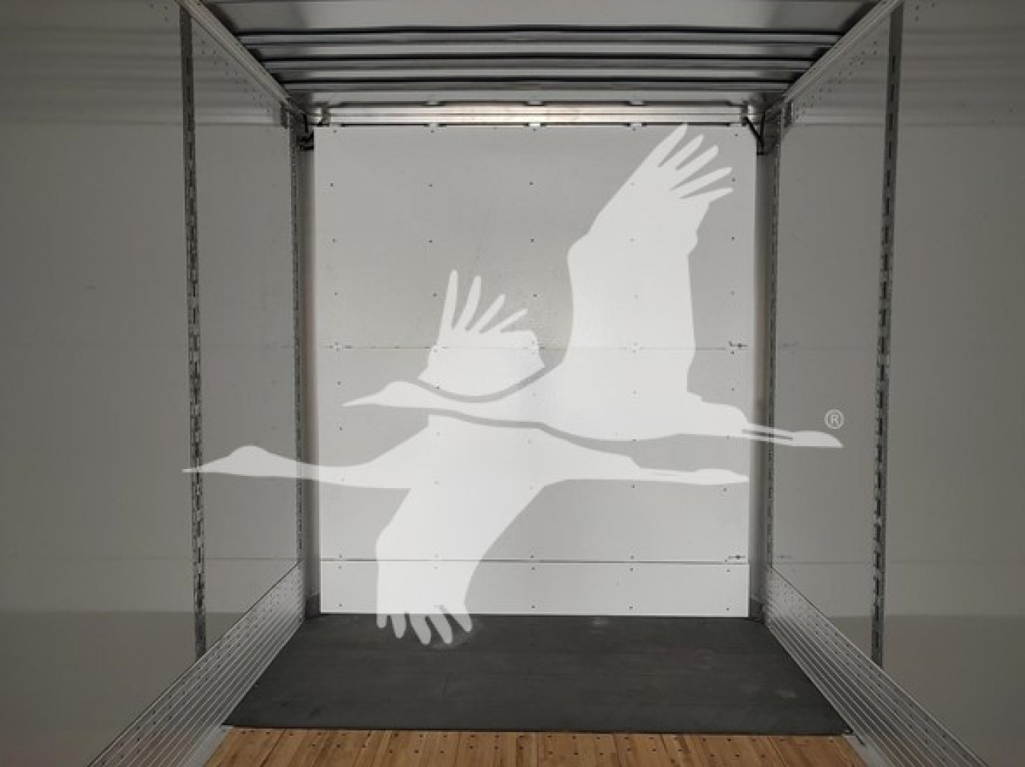 Trailer interior with entry from rear showing bare walls and wooden floor; watermark of flying geese logo overlain.
