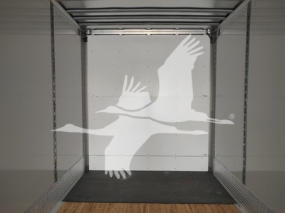 Trailer interior with entry from rear showing bare walls and wooden floor; watermark of flying geese logo overlain.