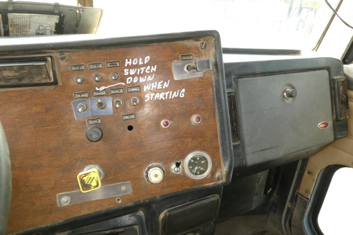 Peterbilt 357 dashboard with wood panel and handwritten controls; switches, gauges, and a note reading 'HOLD SWITCH DOWN WHEN STARTING'