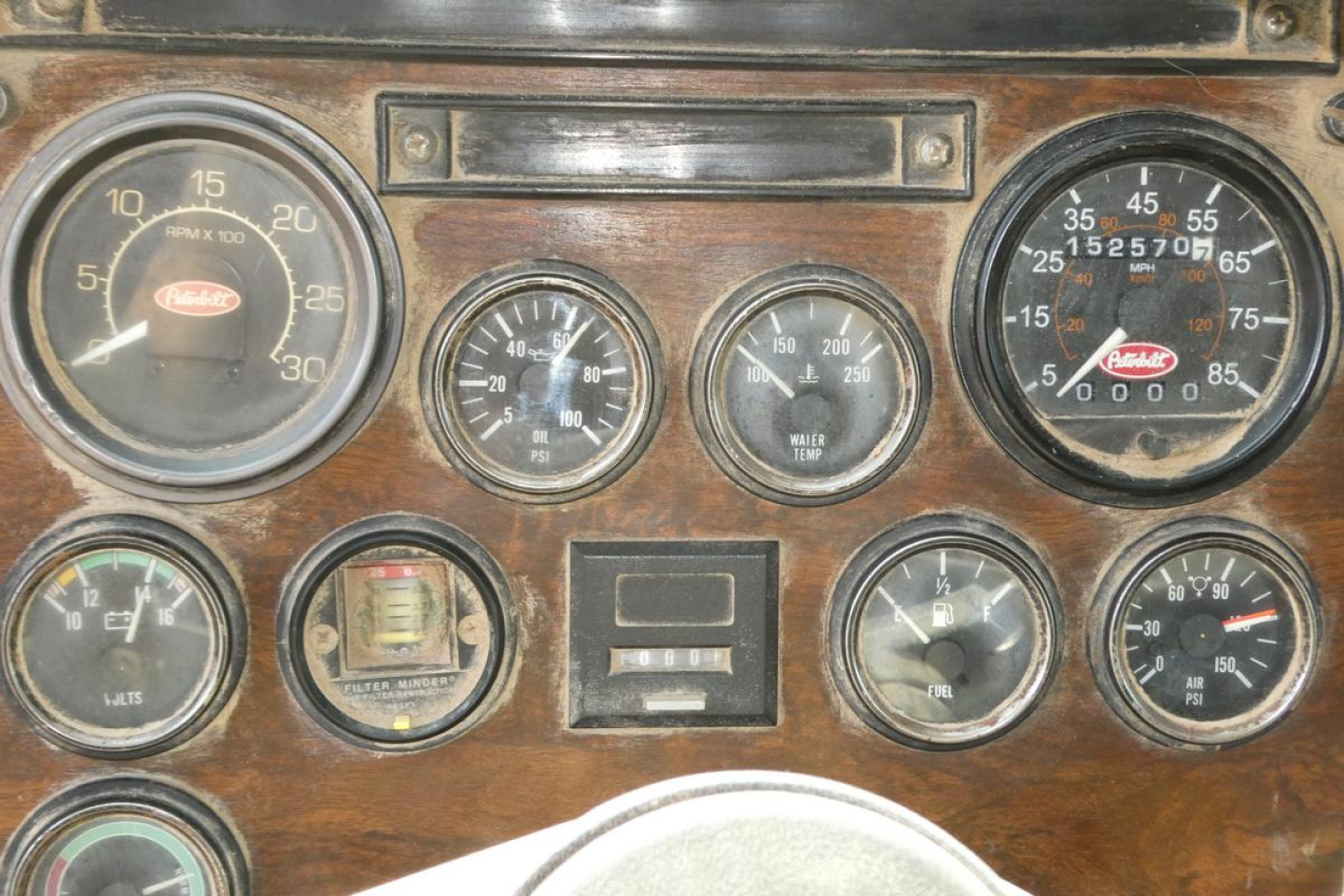 Peterbilt truck dashboard with multiple gauges, wood grain panel, including large tachometer, oil pressure, water temperature, and speedometer cluster.