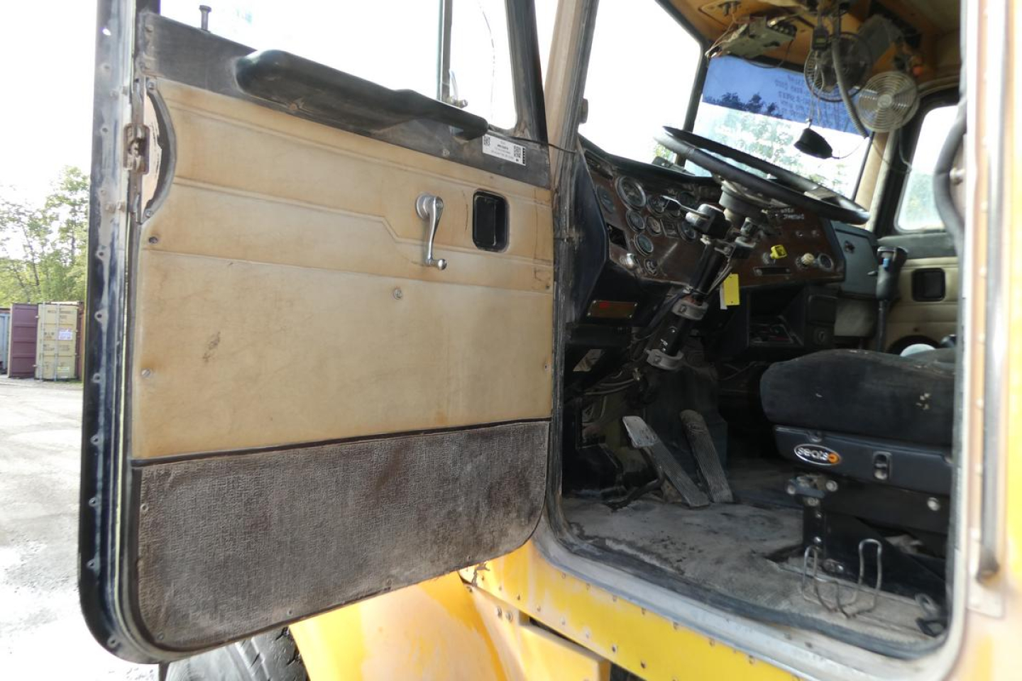 Peterbilt 357 dump truck cab interior and open door showing tan door panel, worn lower trim, and dashboard with steering wheel visible.