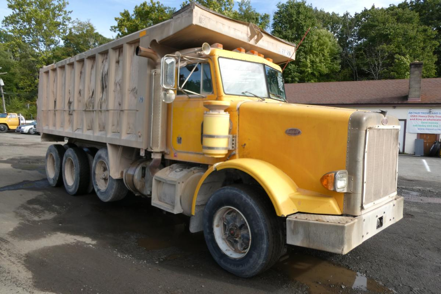 Peterbilt 357 dump truck in yellow showing front cab and dumping bed with multiple rear axles.