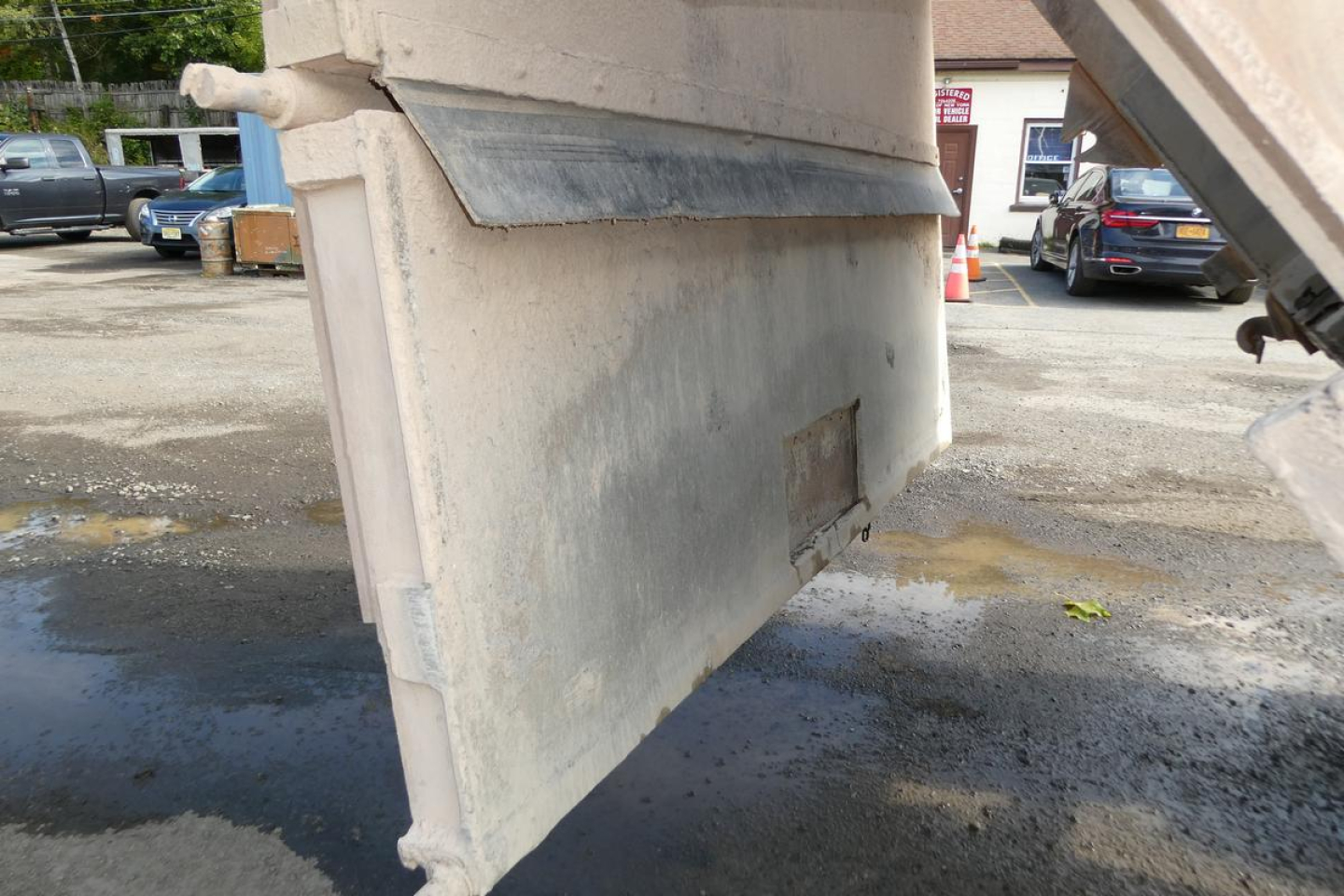 Dump truck bed side/back showing hydraulic tailgate and concrete/dump body surface with dirt and residue.