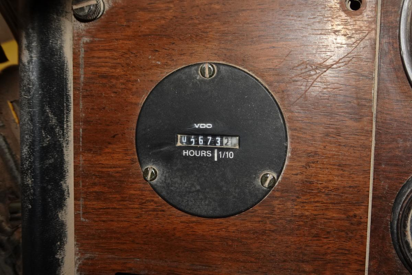 Peterbilt instrument panel showing VDO gauge and hour meter reading 1567? hours on wood panel, circular black gauge with metal screws.