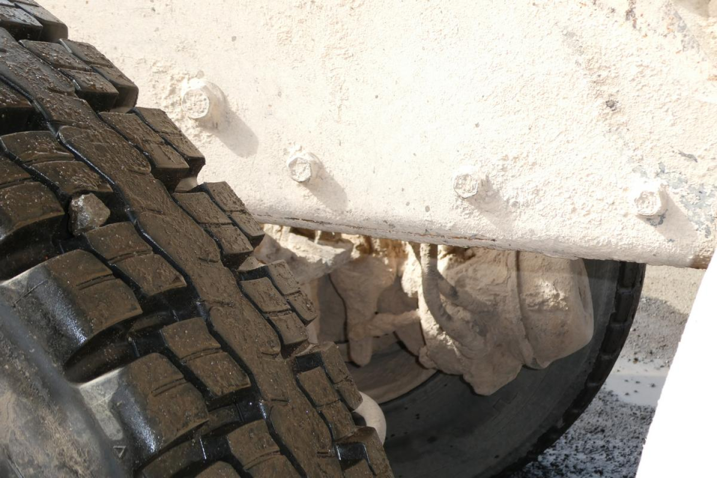 Peterbilt truck wheel and dual tires with undercarriage and mud on white body, partial view of suspension; heavy-duty truck components visible.