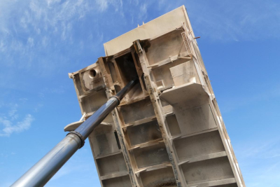Dump truck bed raised by hydraulic cylinder showing metal framework and inner compartments.