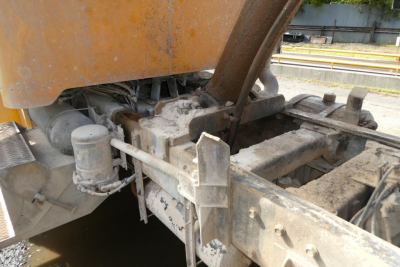 Peterbilt truck chassis area showing hydraulic reservoir, metal framework, and linkage components with orange body paint visible