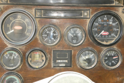 Peterbilt truck dashboard with multiple gauges, wood grain panel, including large tachometer, oil pressure, water temperature, and speedometer cluster.