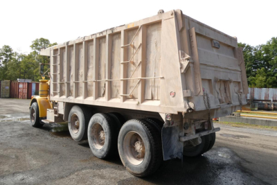 Peterbilt 357 dump truck side/rear view showing large beige dump bed and triple axle rear, VIN sticker area not readable.