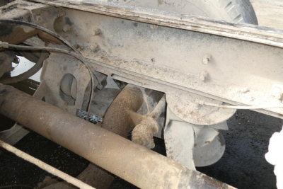 Dump truck undercarriage showing drive line and suspension components with dirt exposure.