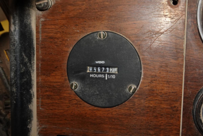 Peterbilt instrument panel showing VDO gauge and hour meter reading 1567? hours on wood panel, circular black gauge with metal screws.