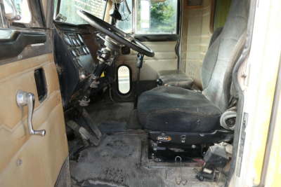 Peterbilt truck interior showing steering wheel, dashboard, and driver seat with entry door on left; worn vinyl seat and floor mat visible.