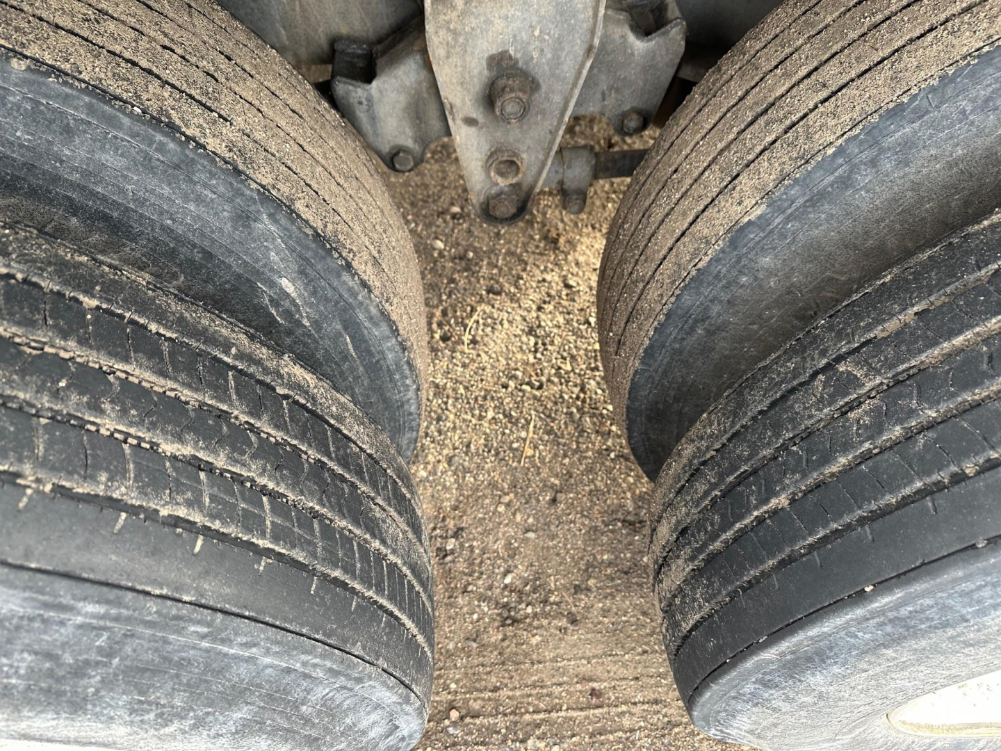 Trailer axle dual tires showing worn tread and gravelly ground between wheels under Fontaine Velocity flatbed trailer.