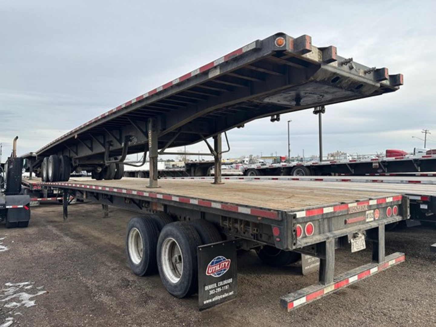 Flatbed trailer showing a raised steel deck on a Fontaine Velocity trailer; rear wheels visible, reflective safety stripes, and tandem axle setup under the deck.