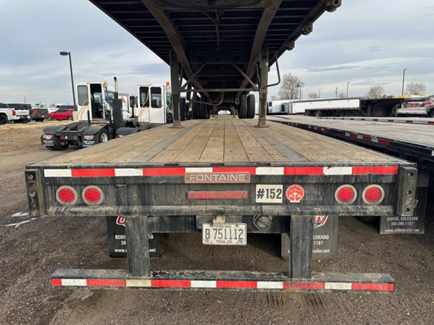 Flatbed trailer rear view showing Fontaine logo, mud flaps, taillights, and license plate under overhang structure.